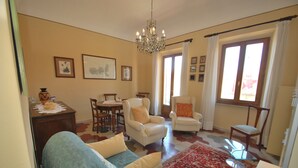 Una sala de estar con una araña, dos sillones, un sofá, una mesa de comedor y una mesa de centro.
