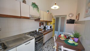 Cocina compacta con estufa a gas, microondas y lavabo. Hay una mesa de comedor con sillas y una planta pequeña sobre la mesa.