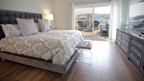 A bedroom with a large bed, a dresser, and a balcony with outdoor furniture. - Charming townhouse with beautiful ocean views and only steps to the beach! (Wrightsville Beach)
