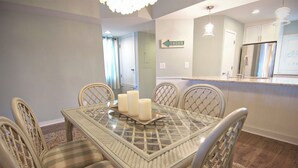 A dining area with a glass-top table, six chairs, and three candles. - Charming townhouse with beautiful ocean views and only steps to the beach! (Wrightsville Beach)