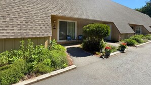 A motel with a sloped roof, a covered patio with chairs, and a well-maintained garden. - Stay at One of the Most Convenient Locations in North Conway, NH! (North Conway)