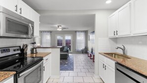 A modern kitchen with white cabinets, a microwave, stove, and sink. There is a dining area with a table and chairs visible through an open doorway. - Island Townhouse w/ Private Hot Tub! (Corpus Christi)