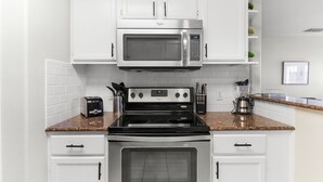 A kitchen with white cabinets, a microwave, a stove, and a toaster. - Island Townhouse w/ Private Hot Tub! (Corpus Christi)