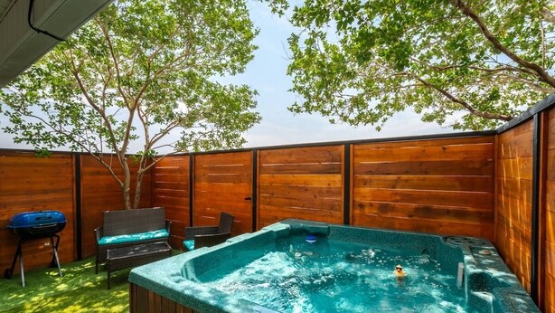 A hot tub in a wooden-fenced backyard with a tree, a grill, and outdoor furniture. - Island Townhouse w/ Private Hot Tub! (Corpus Christi)