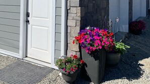 Un edifici amb façana de pedra, porta de garatge numerada i plantes amb flors.
