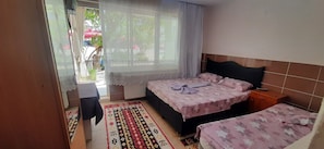 A bedroom with a bed, a nightstand, a window with curtains, a patterned rug, and a view of the outside.