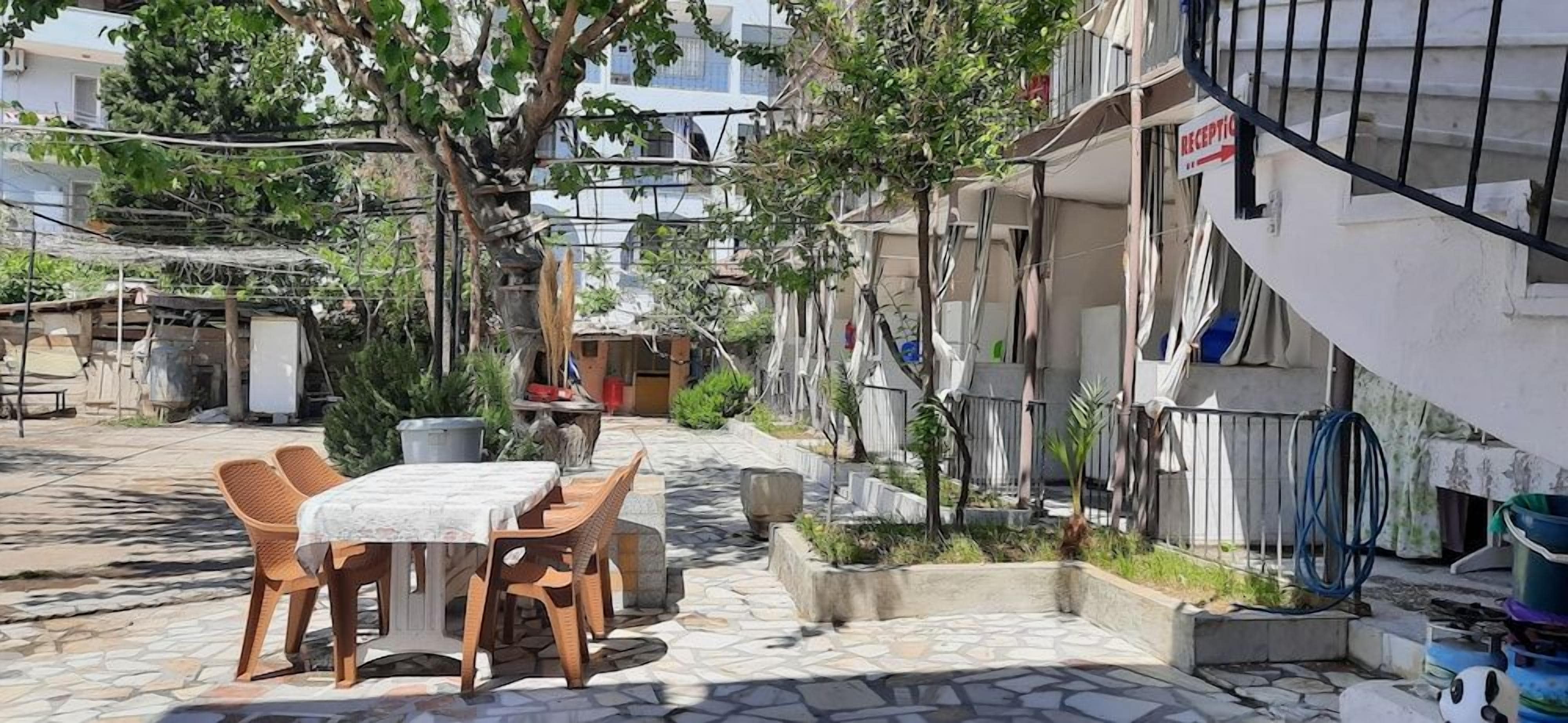 Un área de estar al aire libre con una mesa y sillas, rodeada por un patio empedrado y un edificio con balcón.