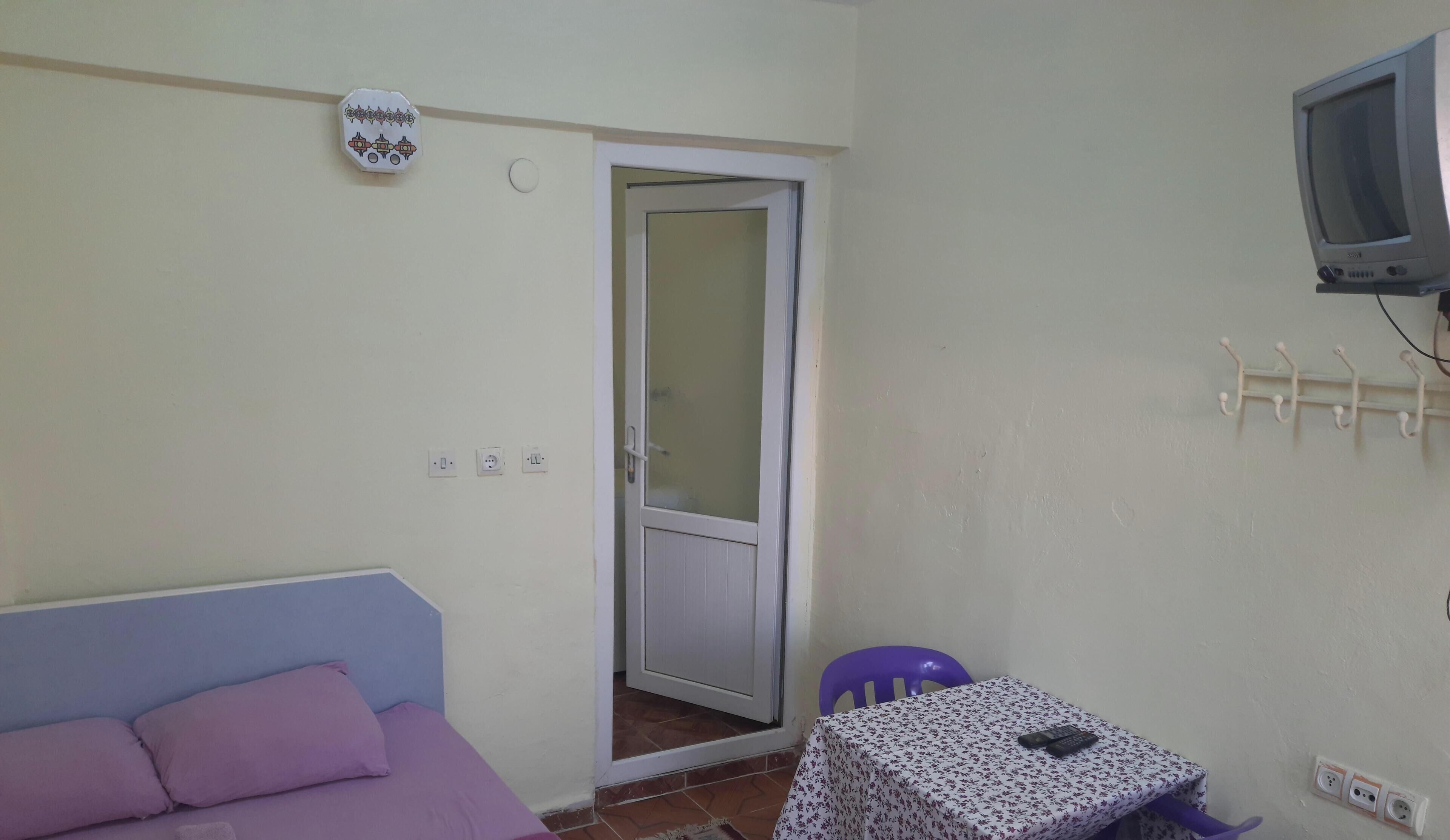 A room with a bed, a table with a floral tablecloth, a television, and a door with a glass panel.