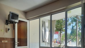 A hotel room with a bed, a desk, a television, and a window with curtains. - Batu Pansiyon (Denizli)