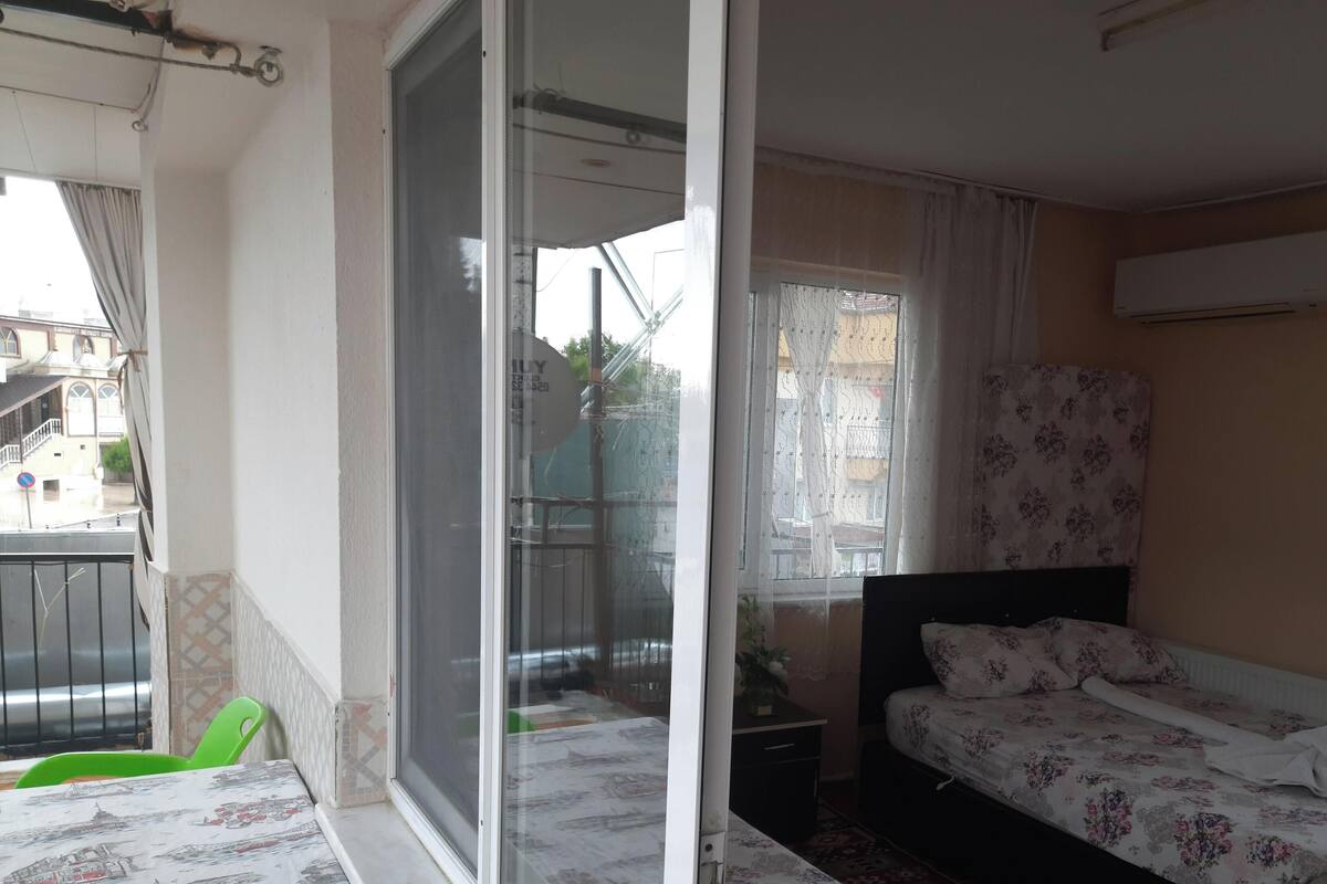 Een slaapkamer met een bed, een raam met gordijnen, een radiator en een balkon met een stoel.