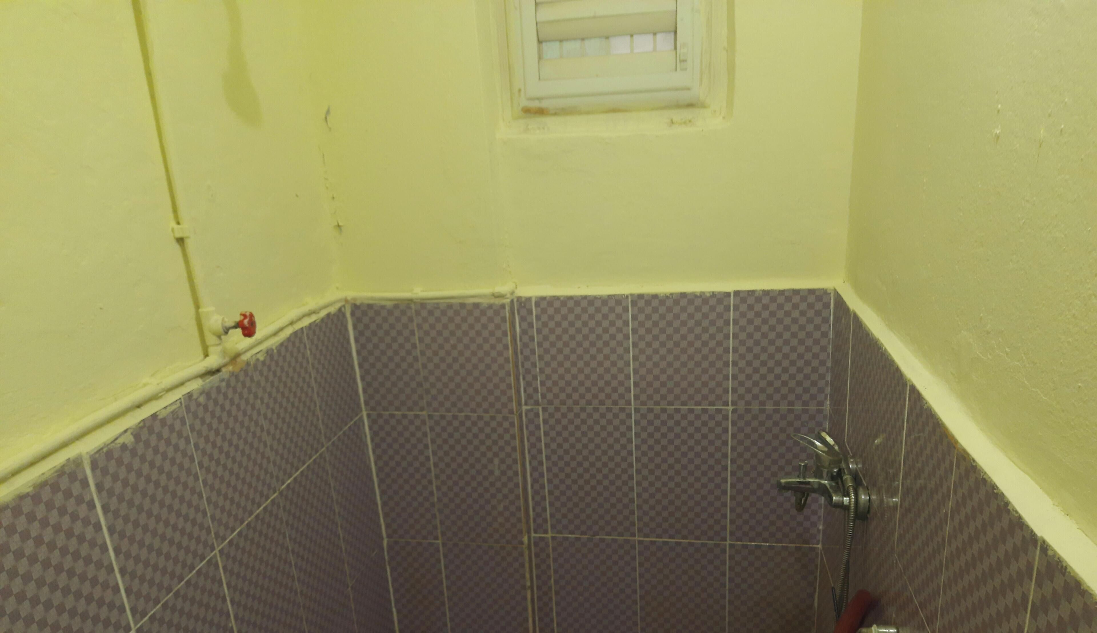 A bathroom with checkered tiles, a shower, and a window with a white frame.