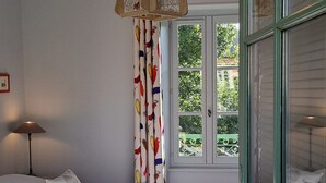 Una camera da letto con un letto, un lampadario, una finestra con tende e vista sul verde circostante.