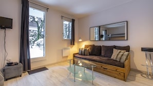 A modern living room with a glass coffee table, a sofa with cushions, a mounted TV, and a large window with curtains. - Perfect for couples, friends and small families. (Chamonix-Mont-Blanc)