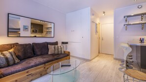 A modern living room with a glass coffee table, a brown sofa, and a kitchen visible through an open door. - Perfect for couples, friends and small families. (Chamonix-Mont-Blanc)