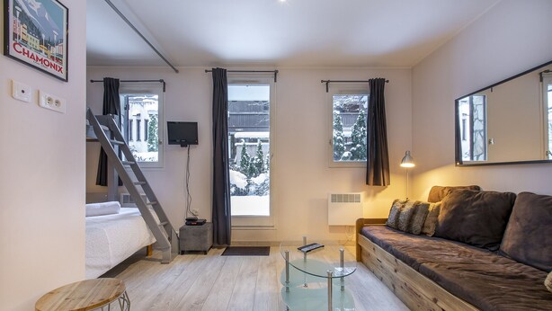 A modern living room with a sofa, a glass coffee table, a TV mounted on the wall, and a staircase leading to another room. - Perfect for couples, friends and small families. (Chamonix-Mont-Blanc)