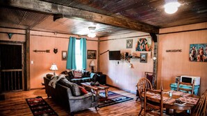 Une pièce rustique avec un plancher en bois, un canapé, une table à manger avec des chaises et un téléviseur fixé au mur.