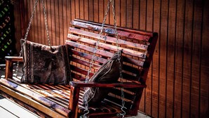 Une chaise suspendue en bois, avec un sac en cuir marron qui y est accroché, le tout maintenu par des chaînes métalliques.