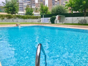 A swimming pool with clear blue water, surrounded by a low wall and a grassy area. - EUROPA APARTMENT R068 (Benidorm)