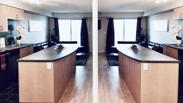 Een moderne keuken met twee keukeneilanden, donkere gordijnen en uitzicht op de woonkamer.