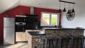 A modern kitchen with a stone island, black bar stools, and a red accent wall. - New house for 2 to 8 people at the foot of the slopes with panoramic view of the lake (Gérardmer)