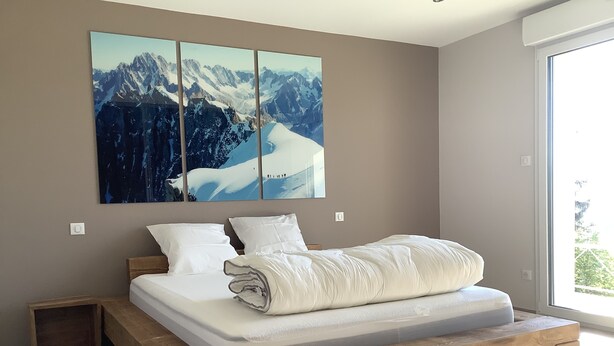 A modern bedroom with a wooden platform bed, white bedding, and a large mountain landscape painting above the bed. - New house for 2 to 8 people at the foot of the slopes with panoramic view of the lake (Gérardmer)