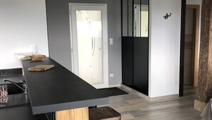 A modern kitchen with a black countertop, wooden stools, and a large window. - New house for 2 to 8 people at the foot of the slopes with panoramic view of the lake (Gérardmer)