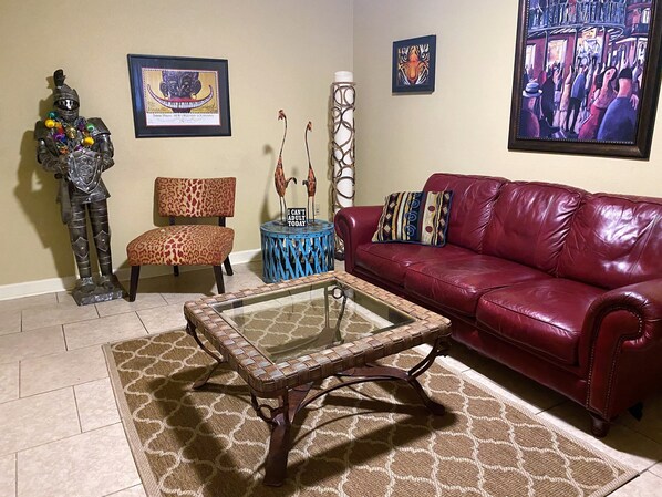 A living room with a red leather sofa, a patterned armchair, a glass coffee table, and decorative items including a framed picture and a sculpture. - Comfortable and Quiet Condo in Perfect LSU/Downtown Area (Baton Rouge)