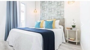 A neatly made bed with a white and navy blue bedspread, two patterned pillows, and a small bedside table with a plant. - innSevilla luxury apartment pilatos, comfort and luxury in this apartment (Sevilla)