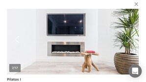A modern living room with a flat-screen TV mounted above a fireplace, a wooden stool with a book, and a large potted plant. - innSevilla luxury apartment pilatos, comfort and luxury in this apartment (Sevilla)