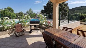 Un patio techado con piscina, mobiliario exterior y vistas del paisaje circundante.