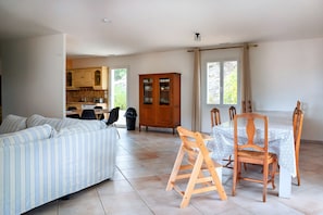 Amplia sala de estar con sofá, mesa de comedor y sillas, un aparador de madera y una cocina al fondo.