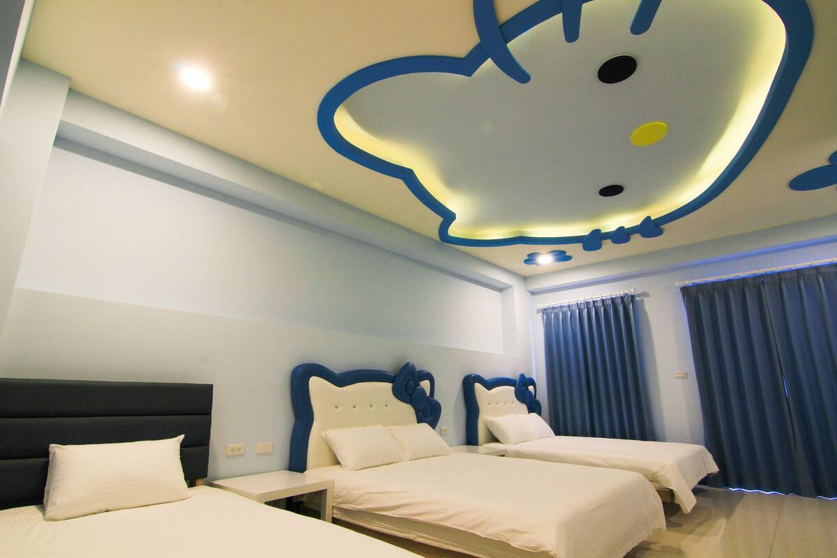 A hotel room with two beds, a ceiling with a Hello Kitty design, and a window with curtains.