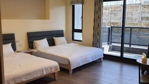 Habitación de hotel con dos camas, un ventanal con vistas a una construcción y una lámpara en el techo.
