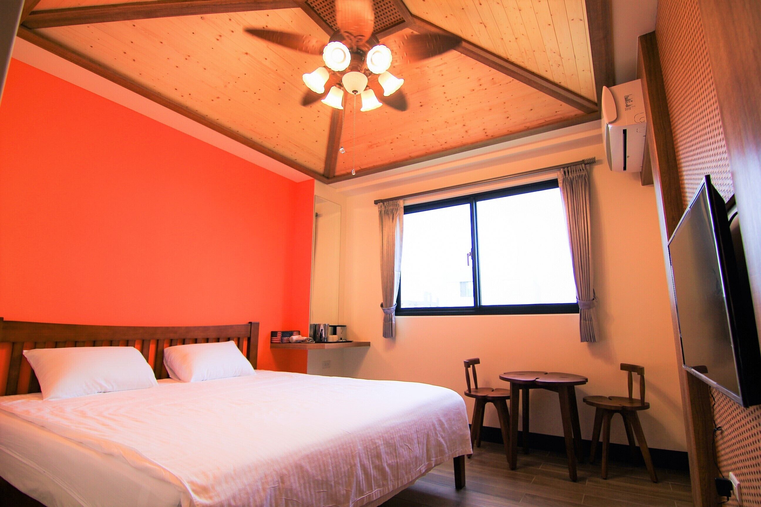 Habitación de hotel con cama, ventilador de techo, ventana con cortinas, una mesita y televisor.