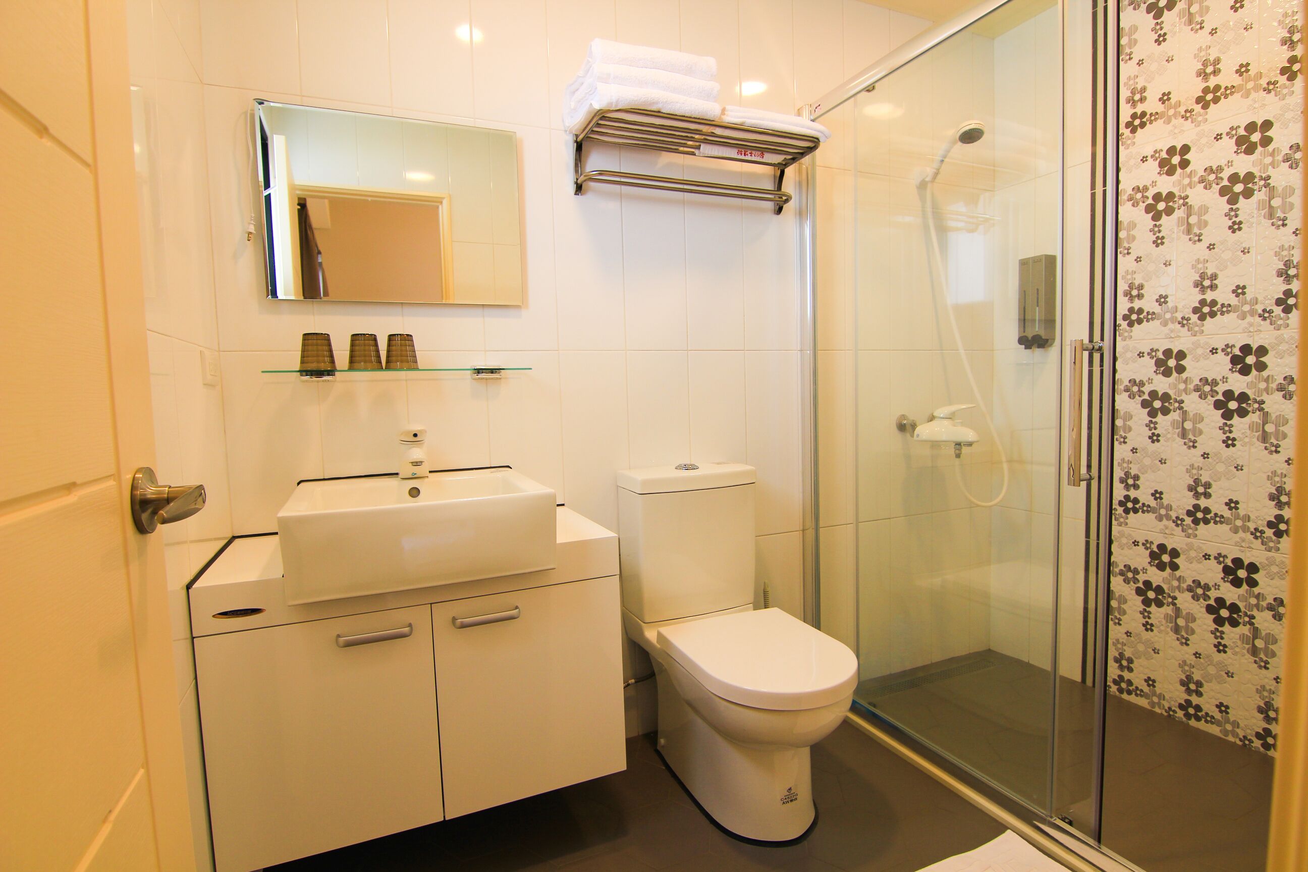 A modern bathroom with a glass shower enclosure, a white toilet, a sink with a mirror above, and a towel rack.