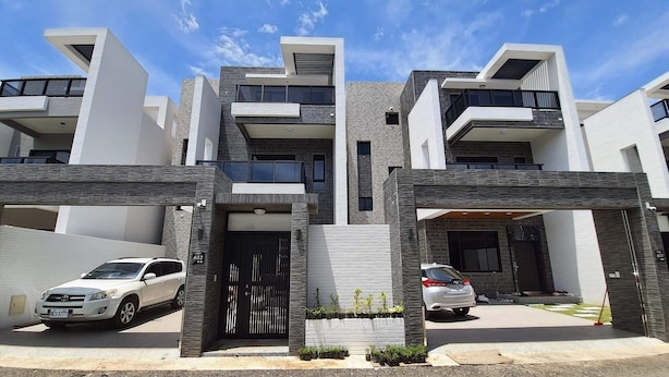 Un edificio residencial moderno de varios pisos con fachada simétrica, ventanas amplias y una entrada central.