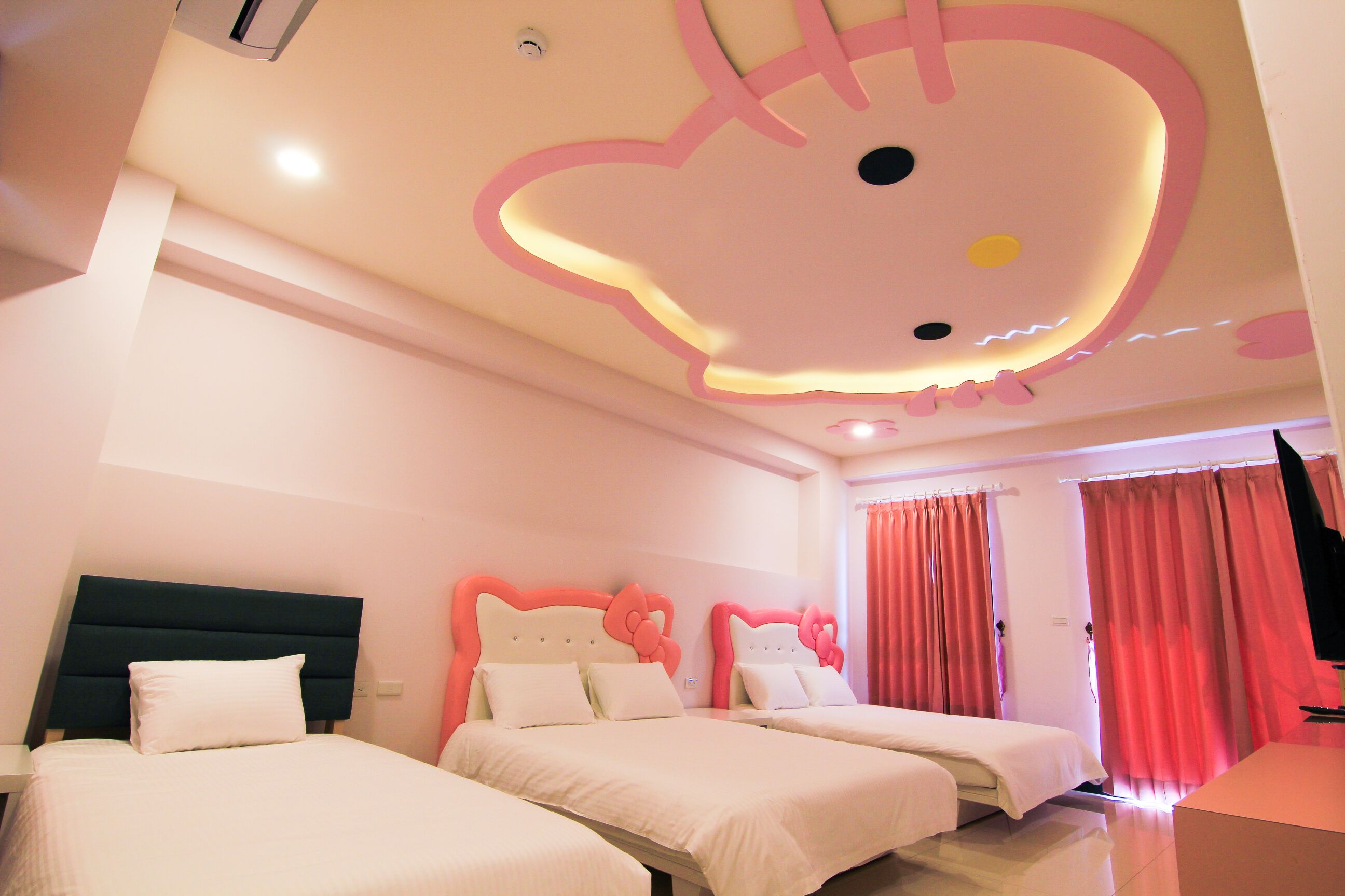 Une chambre d’hôtel avec deux lits, une grande fresque rose représentant Hello Kitty au plafond et des rideaux roses.
