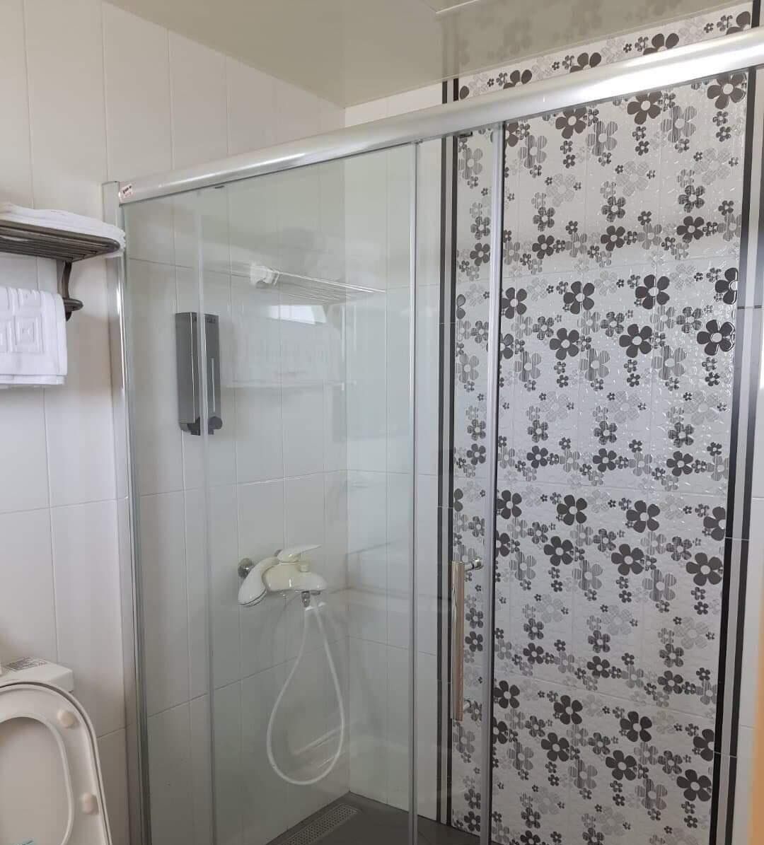 Een douche met glazen wanden, een betegelde muur met bloemenprint, een witte handdoek aan een rek en een handdouche.