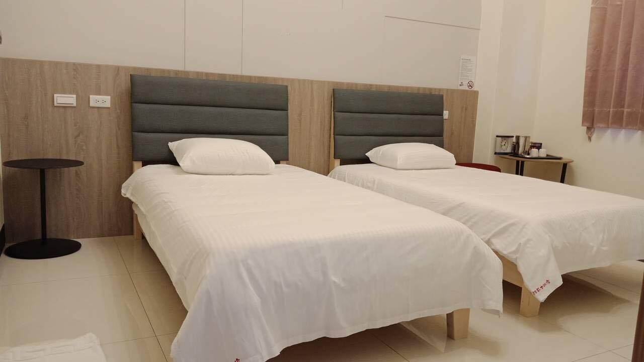 Een hotelkamer met twee enkele bedden, een klein rond tafeltje en een wandplank.