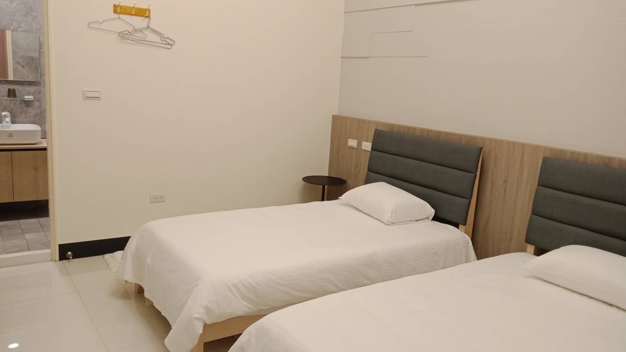 A hotel room with two single beds, a small round table, and a wall-mounted towel rack.
