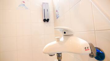 A bathroom with white tiled walls, a white faucet with a blue handle, and a soap dispenser on the wall.