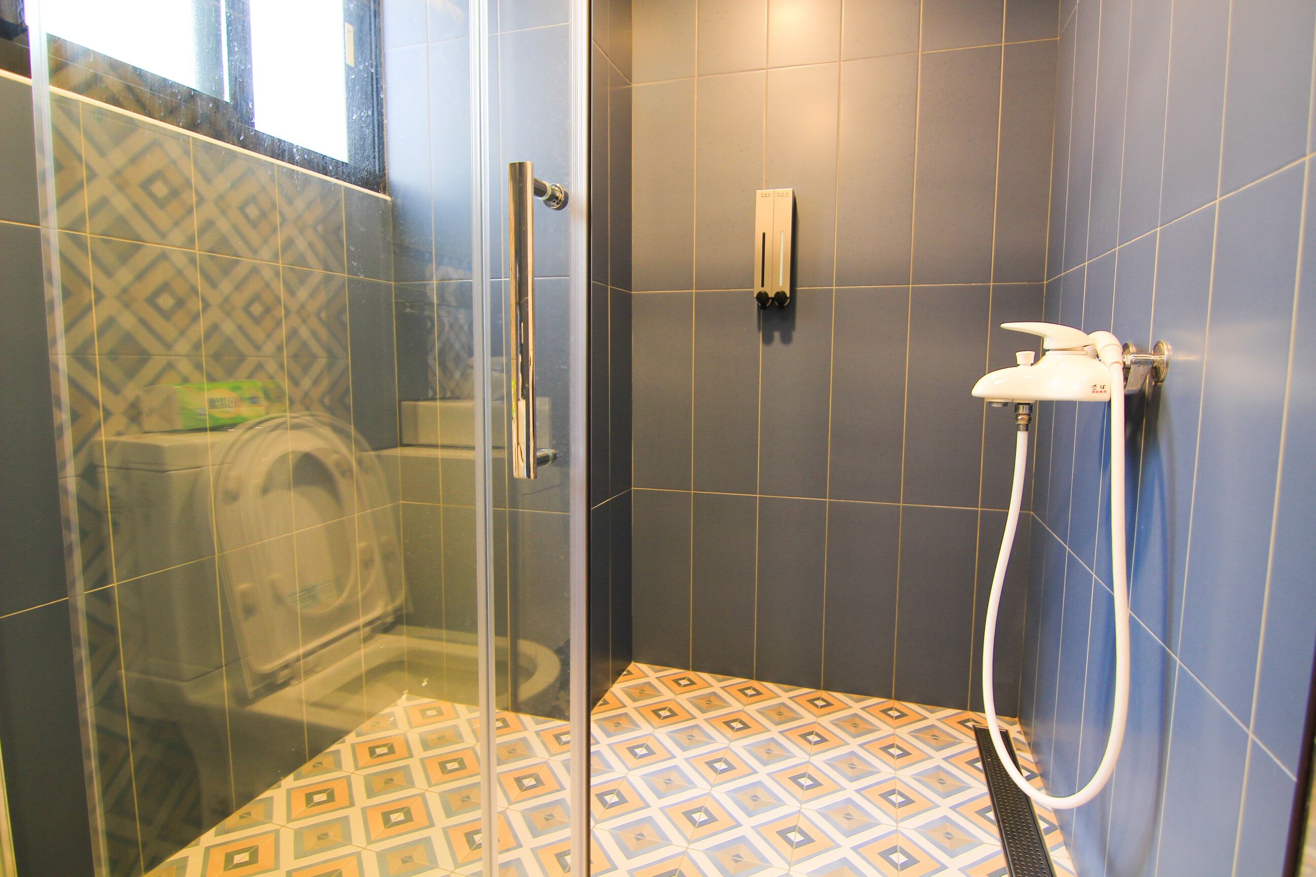 Un espace douche doté d’une porte en verre, d’un pommeau de douche à main et d’un sol carrelé orné d’un motif géométrique.
