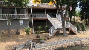 Una propiedad frente al agua con una terraza de madera, un muro de piedra de contención y una escalera que lleva a un balcón.