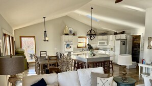 Un salón espacioso con un sofá blanco, una zona de comedor y una cocina con armarios blancos y una isla grande.