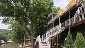 Una terraza de madera de varios niveles con una escalera que conduce a un nivel superior, con vistas a un cuerpo de agua y rodeada de árboles.