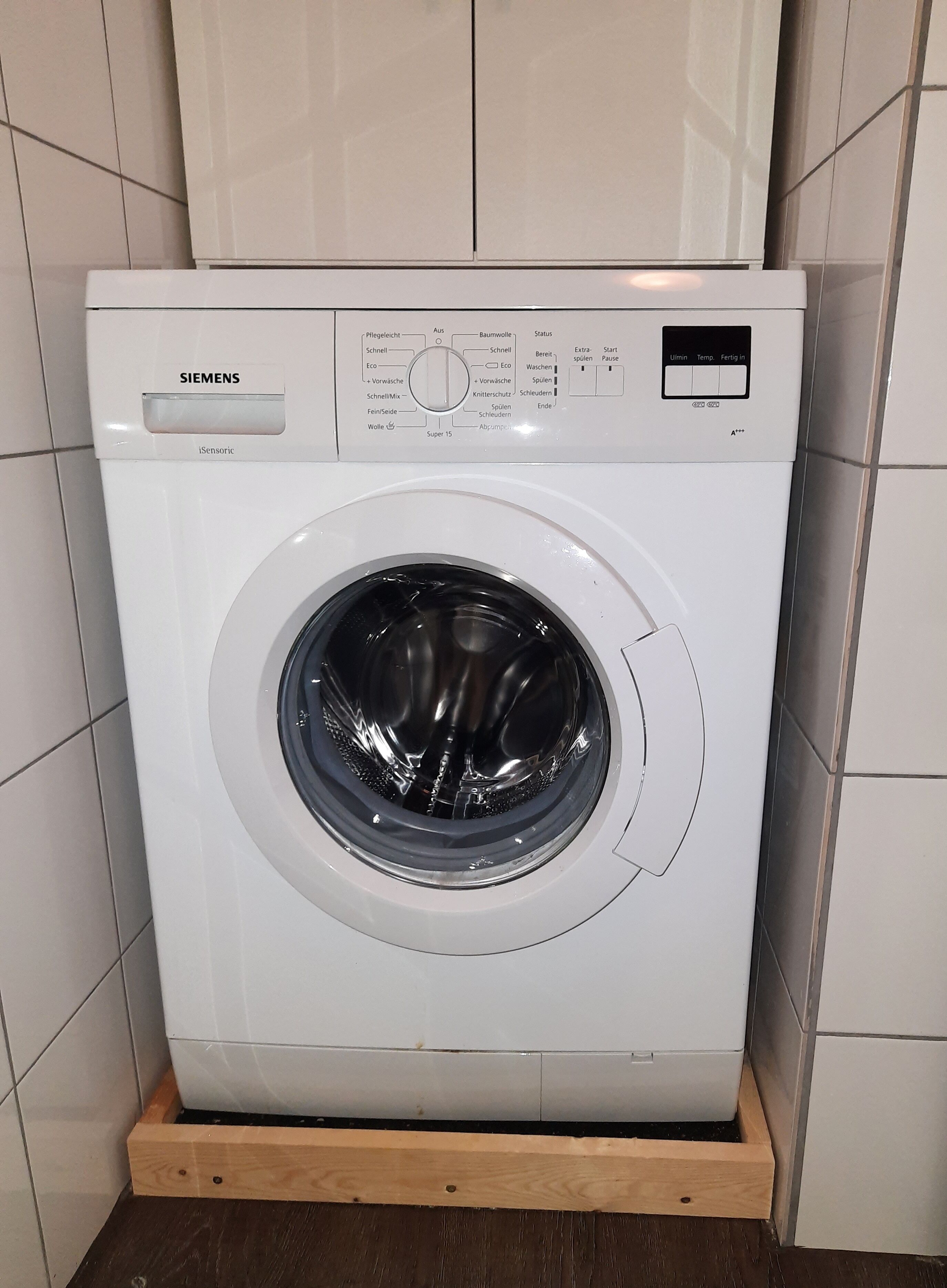 A white Siemens washing machine with a control panel and a wooden base.