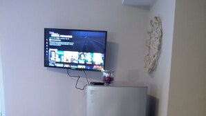 A small room with a bed, a refrigerator, and a wall-mounted TV displaying a streaming service interface. - studio on  Swanston st apartment with a little English flare (Carlton)