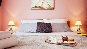 A hotel room with a bed, two bedside lamps, a painting of a sailboat, and a tray with a donut and coffee cups. - Comfortable apartment  (Pozzallo)
