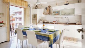 A modern kitchen with white cabinets, a dining table set for four, and a view of the outside balcony. - Comfortable apartment  (Pozzallo)