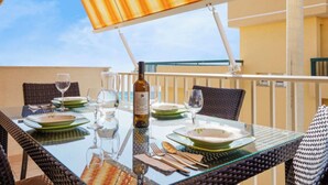 An outdoor dining area with a glass table, wicker chairs, and a striped awning. - Comfortable apartment  (Pozzallo)